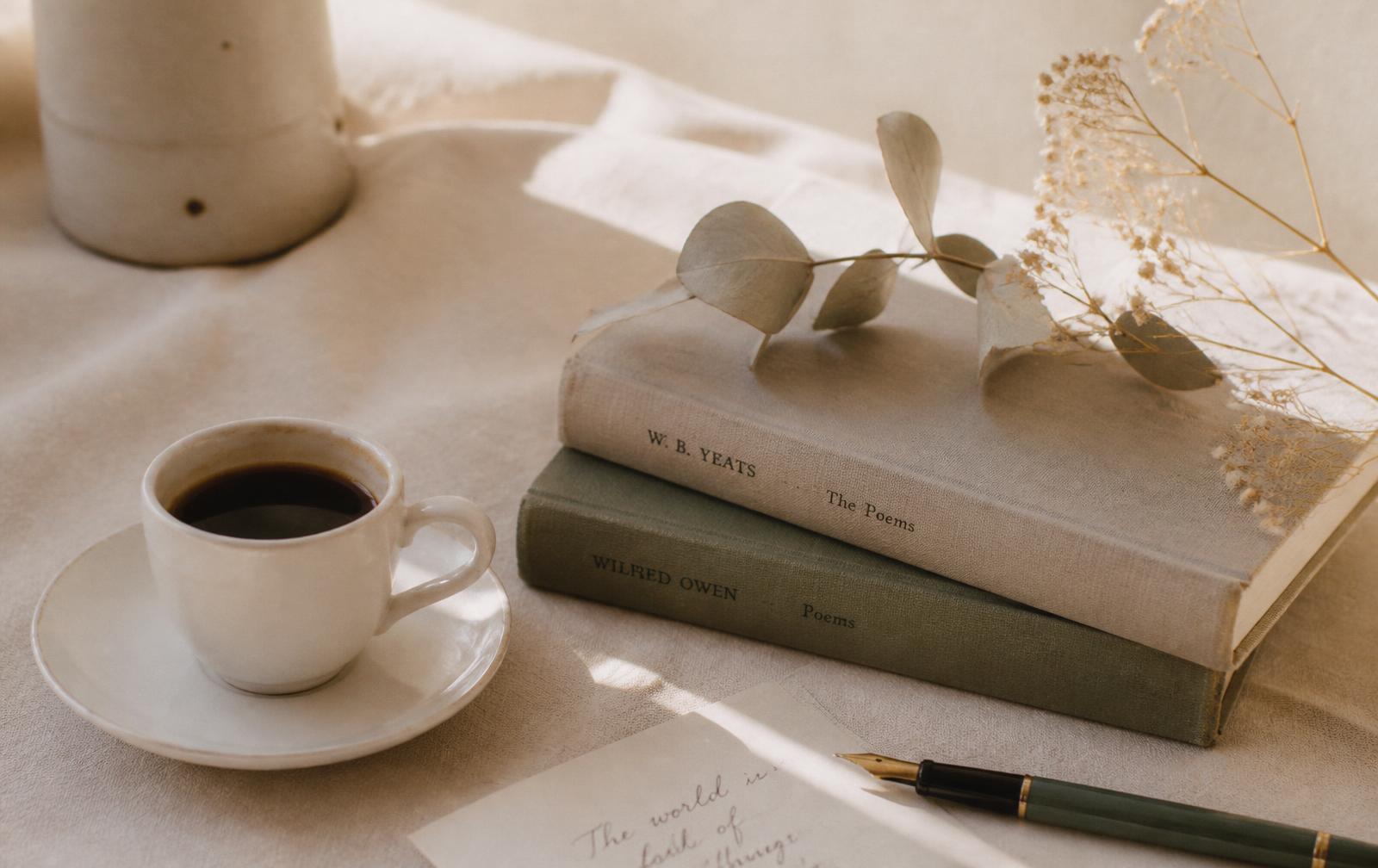 Xícara de café, livros de poesia e ramos secos sobre linho claro